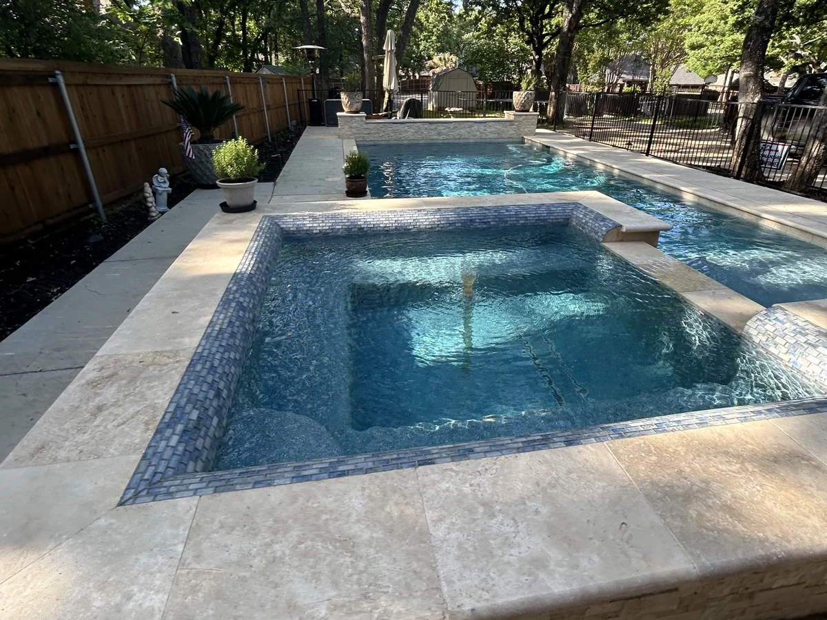 Raised spa and rectangular swimming pool bordered by light coping and mature trees.
