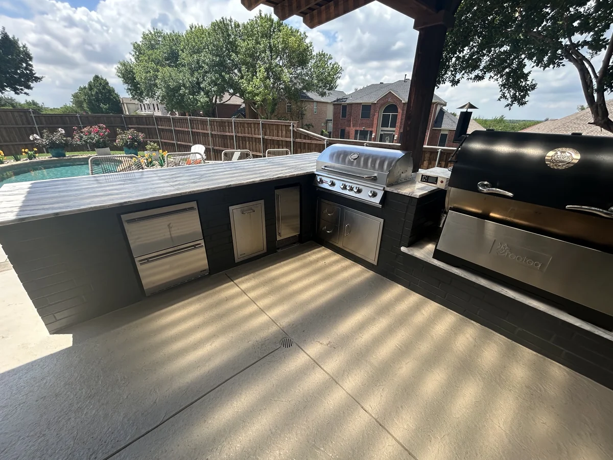 Outdoor kitchen and counter beneath a timber pergola beside a swimming pool.