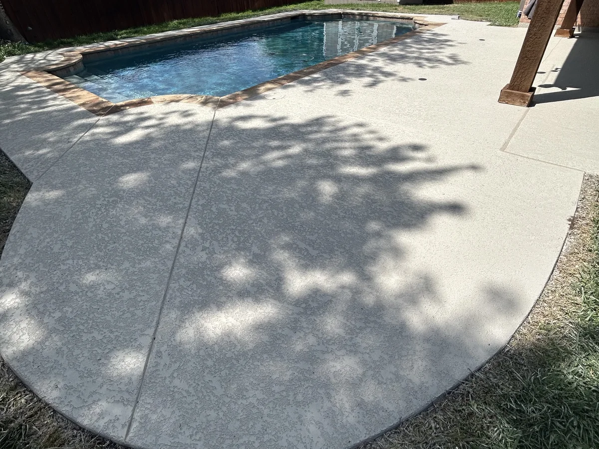 Light-colored pool decking curving around a swimming pool.