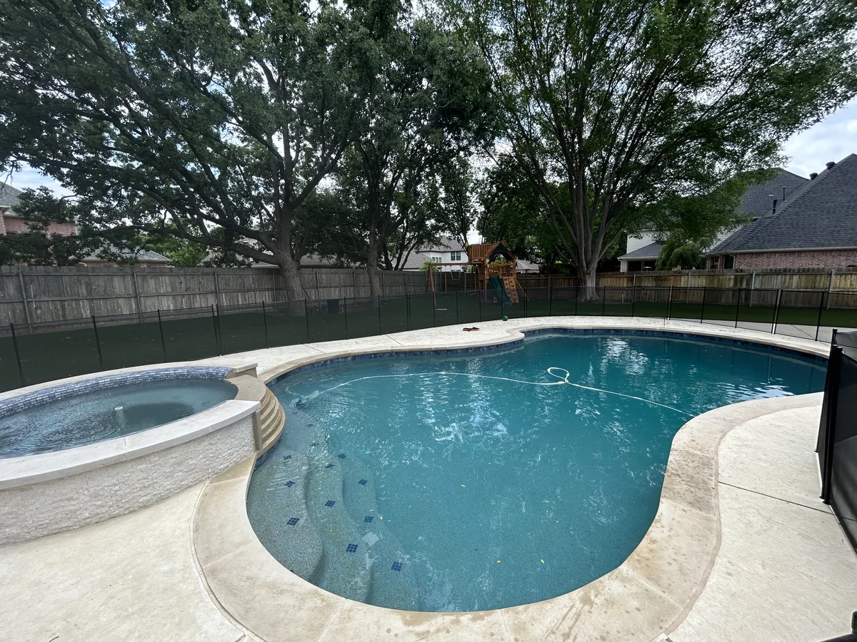 Curved swimming pool and round raised spa beside light-colored decking.